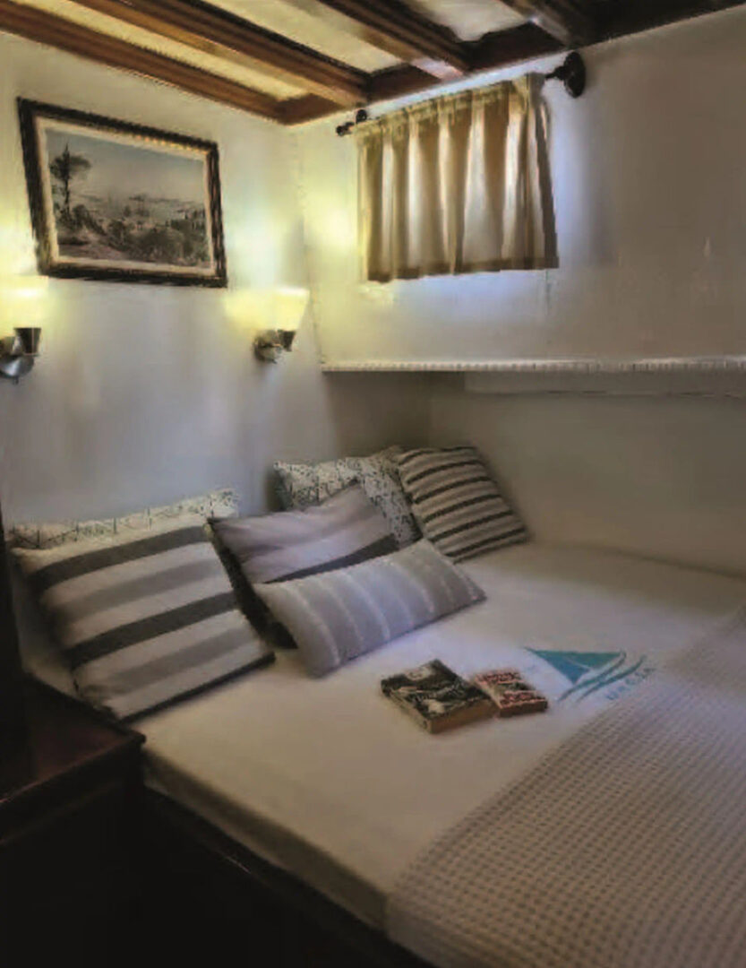 Comfortable cabin with plush bedding and decor inside a traditional wooden boat, part of Events on Board's Saronic Gulf cruise.